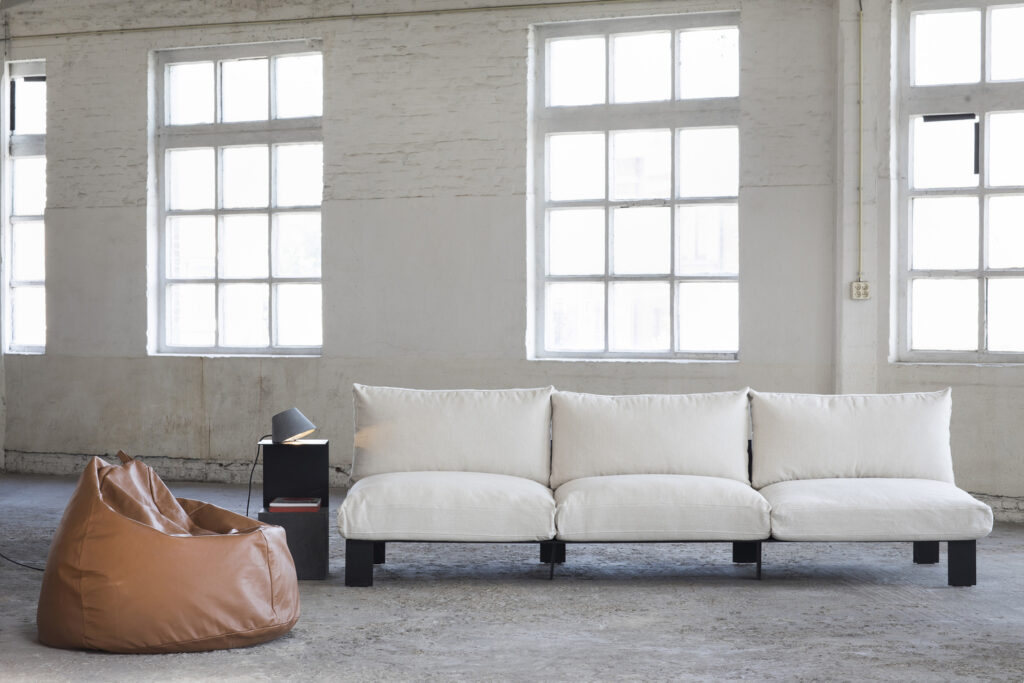פוף גדול בגוון טבעי לצד ספה תלת-מושבית לבנה, בעיצוב SERAX, בלגיה