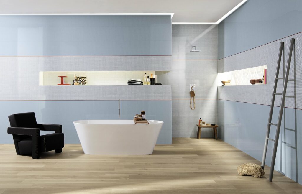 חיפוי קירות בקרמיקה באפור ובתכלת, רצפת שיש בגוון טבעי ואמבטיית פרי סטנדינג לבנה, בעיצוב FAP CERAMICHE, איטליה