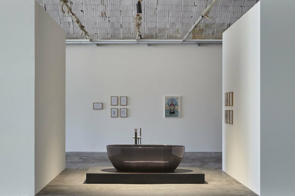 חלל אמבטיה מינימליסטי עם במת שיש נמוכה ועליה אמבט פרי סטנדינג מזכוכית חומה, בעיצוב "אנטוניו לופי", איטליה