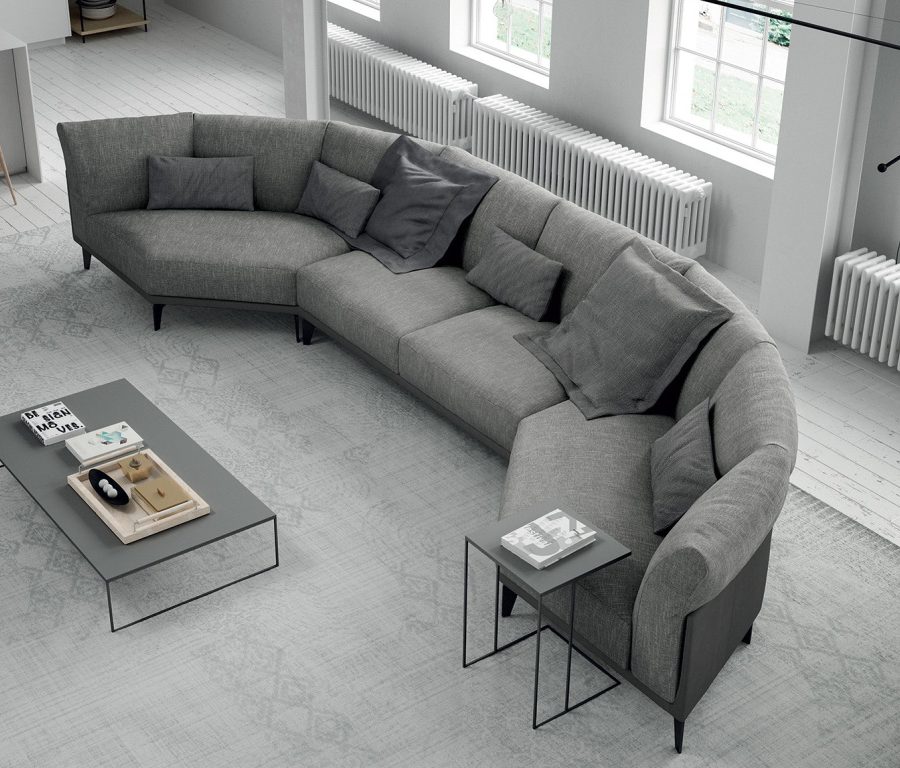 ספה בצורת חצי מעגל, מרופדת באריג אפור, וכריות בגוונים שונים של אפור, בעיצוב Doimo Salotti